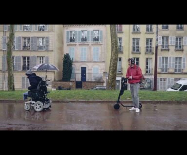 Escena de corto Électrique. Dos personas en una calle, a la izquierda una persona usuaria de silla de ruedas y a la derecha una persona de pie junto a un scooter.