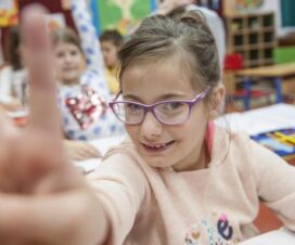 Niña con discapacidad saludando realizando el símbolo de la paz con su mano, en una sala de clases. Fuente: UNICEF/Pancic