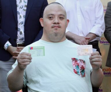 Hombre con síndrome de Down muestra dos carnets de vacunación, uno en cada mano.
