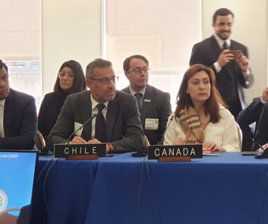 Defensor Nacional, Carlos Mora Jano, sentado junto a otras personas en salón de OEA.
